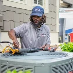 Technician servicing an air conditioning unit outside a home with a Trane vehicle in the background.