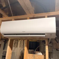 White Daikin wall-mounted air conditioner installed in an unfinished wooden frame room with exposed ceiling beams.