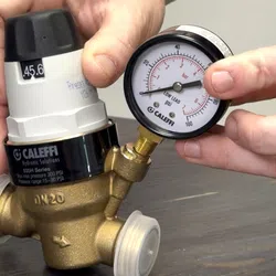 Hands adjusting a Caleffi pressure gauge attached to a brass hydraulic valve on a wooden surface
