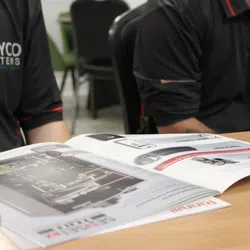 Two people in black Dayco Systems shirts reviewing an information catalog on Rinnai Water Heaters.