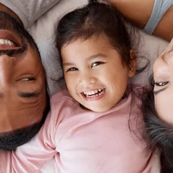Happy family of three lying down together smiling, showing close bond and joyful moments
