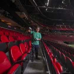 Worker wearing green shirt sprays disinfectant in empty stadium seating before event