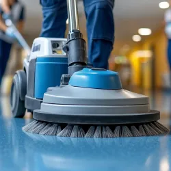 Close-up of a floor cleaning machine polishing a shiny blue floor with workers in background.