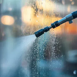 Close-up of a high-pressure water spray cleaning a glass window with blurred lights in the background