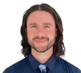Smiling man with curly hair wearing a navy blue shirt and striped tie against a white background.
