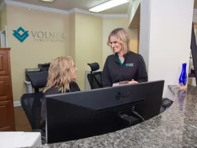 Two female dental office staff smiling and interacting behind a reception desk at Volner Family Dental.