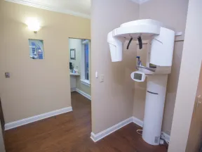 Dental panoramic X-ray machine in a clean, modern dental office with wood flooring and beige walls.