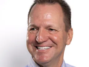 Smiling middle-aged man with short hair wearing a light blue striped shirt against a white background