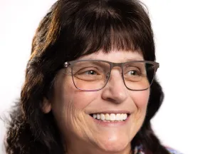 Close-up of a smiling woman with glasses and dark hair against a white background.