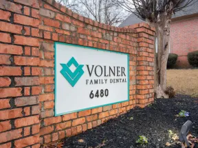 Brick sign for Volner Family Dental with teal logo and address 6480 in a landscaped yard.