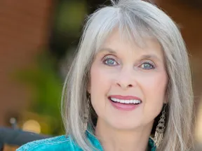 Smiling mature woman with gray hair and blue eyes wearing turquoise top and dangling earrings outdoors