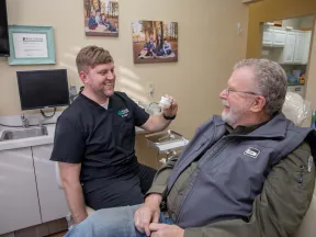 Dentist showing dental mold to a smiling elderly male patient in a bright dental office.