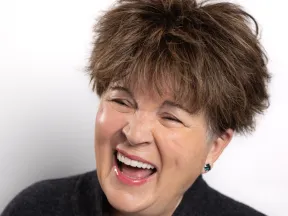 Middle-aged woman with short brown hair laughing joyfully against a white background.