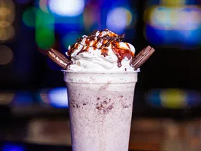 Cookies and cream milkshake topped with whipped cream, chocolate drizzle, and Oreo cookies in a clear cup.