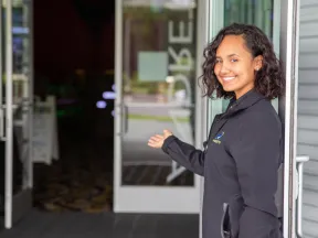 Smiling staff member welcoming guests at an entrance, showcasing hospitality in a vibrant environment.