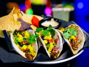 Three soft tacos with grilled chicken, mango salsa, and cilantro served with tortilla chips and dipping sauce.