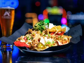 Plate of loaded nachos topped with shredded chicken, jalapenos, sour cream, and cilantro with a beer glass in background.