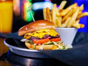 Cheeseburger with lettuce, tomato, and grilled beef patty served with a side of golden French fries and a drink.