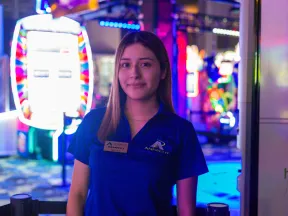 Smiling female staff member in blue Andretti uniform stands in colorful arcade with vibrant lights
