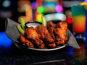 Spicy chicken wings served with celery sticks and ranch dipping sauce on a plate with colorful blurred background.