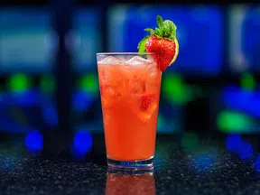 Refreshing strawberry cocktail with ice, garnished with mint and a strawberry, set against a vibrant blue background.