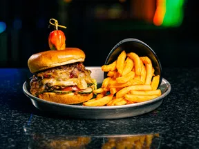 Juicy cheeseburger topped with a pepper and a side of crispy French fries on a metal tray.