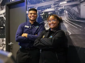 Two smiling employees posing confidently in a modern work environment with industrial decor.