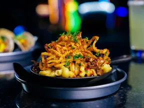 Creamy macaroni and cheese topped with crispy fried onions and fresh herbs served in a black skillet.