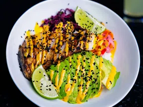 Grilled fish and sliced avocado drizzled with orange sauce, garnished with lime wedges and black sesame seeds