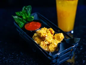 Basket of crispy fried cheese bites served with red dipping sauce and fresh basil with a glass of orange juice.