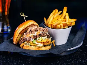 Juicy burger with shredded meat, lettuce, and sauce served with a side of golden French fries on a black plate.