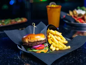 Burger with lettuce, tomato, onions, premium bun, French fries on black tray with drink blurred background