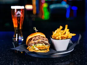 Juicy burger with lettuce, fried chicken, shredded beef, crispy fries, and a glass of beer on a dark table.