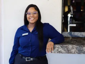 Smiling woman in a blue shirt standing by a counter, showcasing a friendly customer service atmosphere.