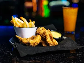 Crispy fried chicken tenders served with French fries and dipping sauce on a black tray.