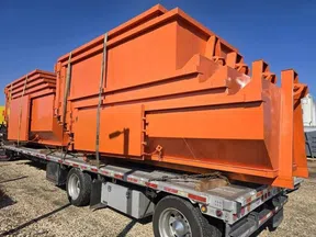 Bright orange industrial scrap metal containers secured on a flatbed trailer under clear blue sky.