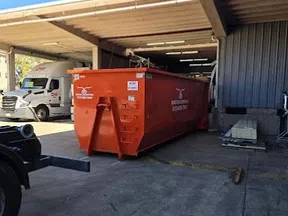 Large orange dumpster container parked outside an industrial building with a truck and loading area visible.