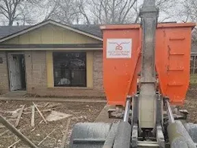 Construction site with orange equipment in front of a single-story house with bare trees in the background