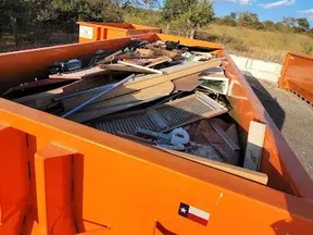Orange dumpster filled with wood debris and construction waste outdoors on a sunny day.