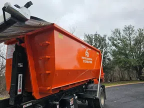 Large orange dumpster trailer with Austin Dumpsters branding parked on a driveway near trees and cloudy sky.