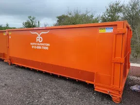 Bright orange Austin Dumpsters container with contact number on gravel surface outdoors.