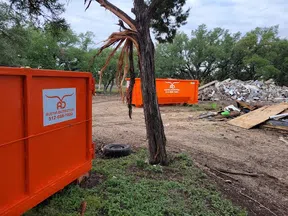 Two bright orange Austin Dumpsters at a debris cleanup site with trees and rubble in the background