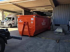 Large orange dumpster container parked in an industrial loading dock area on a sunny day.