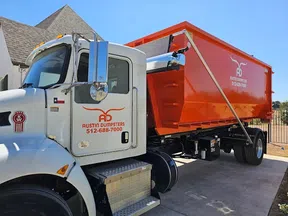 White and orange Austin Dumpsters truck parked outdoors under clear blue sky near a residential area.
