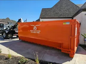Large orange Austin Dumpsters container parked beside a residential driveway under clear blue sky