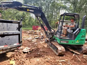 Man operating green 60G excavator from Sunbelt Rentals clearing debris at a construction site with dirt and trees.