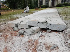 Broken and cracked concrete sidewalk in front of house ready for repair or replacement work.