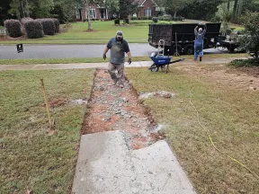 Construction workers break up a concrete sidewalk in a residential front yard for replacement.