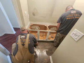 Two workers dismantling a bathroom vanity during demolition and removal services in a home.