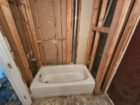 Bathtub installed in unfinished bathroom with exposed wall studs and plumbing pipes